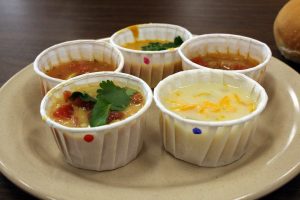 Five paper cups full of different soups