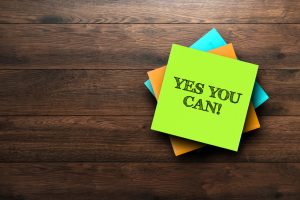 Phrase "yes you can" written on multi-coloured sticky notes on a dark wood background