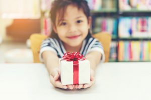 small girl offers a white gift box tied with red ribbon