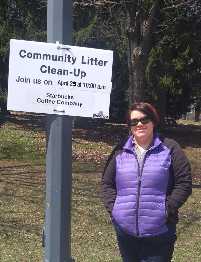 Woman wearing sunglasses stands nest to a community cleanup sign attached to a lamppost
