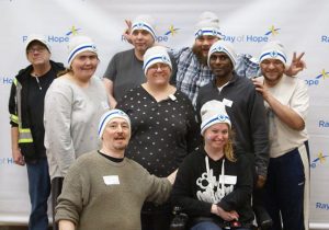 A group of volunteers wearing Coldest Night toques stand in front of the Ray of Hope backgrop
