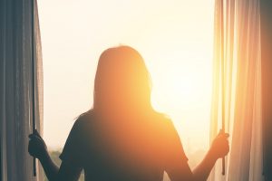 Silhouette of a young woman looking out a window at sunrise