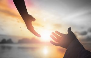silhouette of two hands reaching toward each other against a rising sun