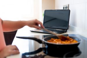 Closeup of hands stirring a pan with a laptop in the background