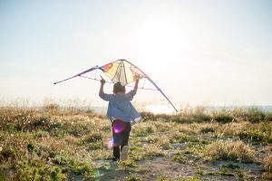 little boy running with kite above his head towards horizon