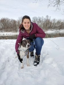 Kate kneels next to a brown and white dog in a snowy field