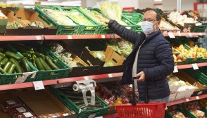 A middle-aged man wearing a medical mask buying food in a grocery store.