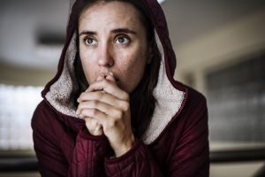 A young woman wearing a hoodie holds her folded hands to her mouth