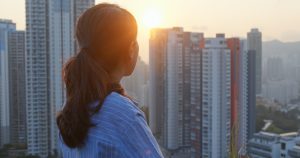 A young woman looks toward the sunrise over high-rise buildings