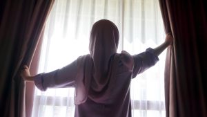 A woman wearing a head scarf opens a window