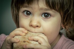 Little girl looks at the camera as she eats bread