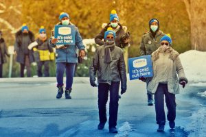 A group of people wearing Coldest Night toques and holding signs walk down a street toward the camera