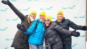 Four women in yellow Coldest Night toques wave at the camera