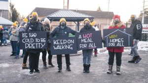 Four women in yellow Coldest Night toques hold signs encouraging walkers