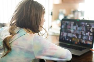 Teenage girls leans toward a laptop displaying a Zoom meeting