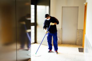 A man wearing a surgical mask mops a hallway