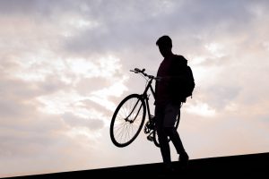Silhouette of a young man carrying bike down the stairs