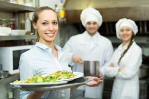 Female server and chefs standing in a restaurant kitchen