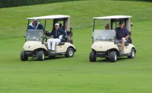 Four men riding in two golf carts over a golf green