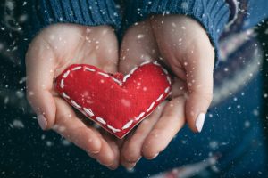 Woman's hands holding a stitched red heart as snow falls