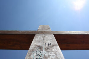 The crossbeam of a wooden cross stretches across the blue sky