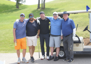 A group of men wearing golf gear stand next to a golf cart