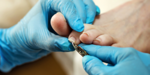 Hands wearing blue gloves trim a person's toenails
