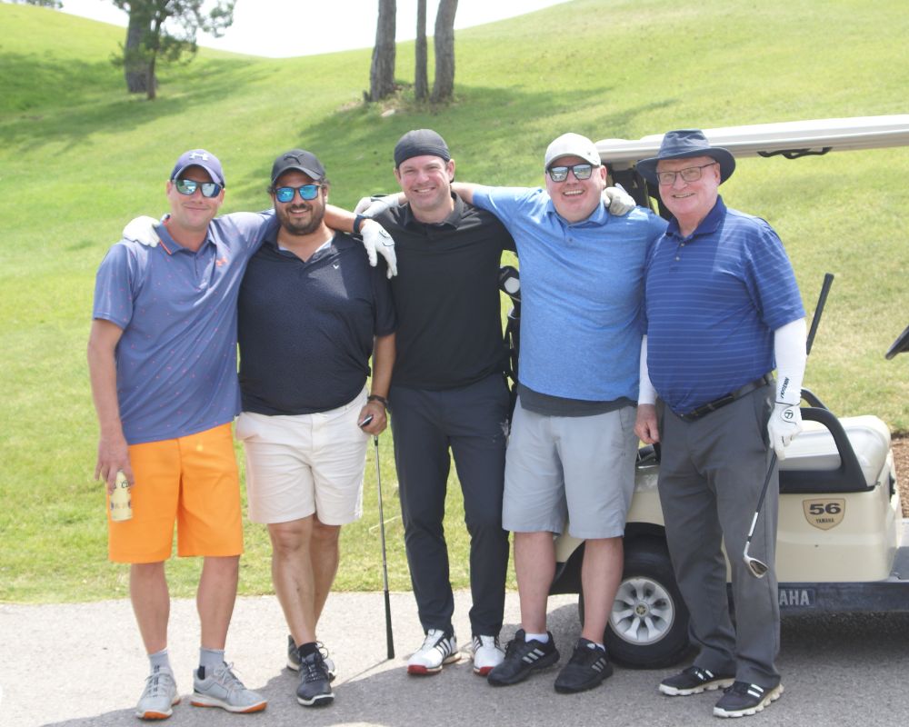 Five smiling men wearing golf gear stand in front of a golf cart